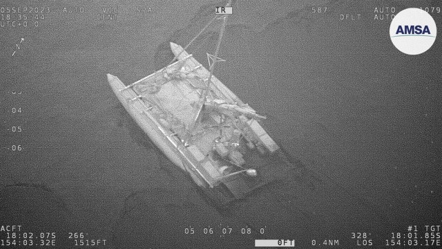 A partially submerged catamaran is shown during a rescue of 3 sailors in the Coral Sea