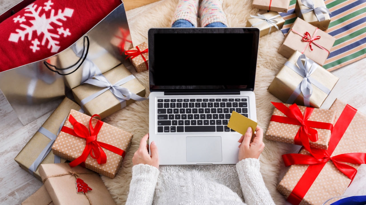 Person shopping on laptop with credit card surrounded by wrapped gifts