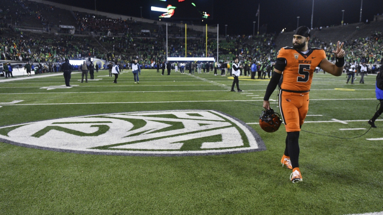 Oregon State quarterback DJ Uiagalelei walks by the Pac-12 logo on a football field.
